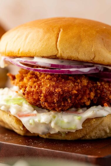 A close up of a golden crispy fried fish sandwich with coleslaw, sliced red onions, and mayonnaise on a soft bun to show off the ultra crispy panko coating.