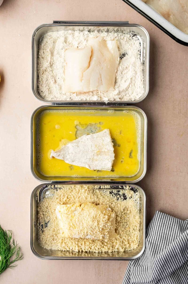 Three trays show fish fillets being coated: one in flour, one in beaten egg, and one in breadcrumbs, arranged in a sequence for breading.