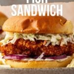 Close-up of a crispy fried fish sandwich with coleslaw and red onion on a bun, with text promoting a recipe on girlcarnivore.com.