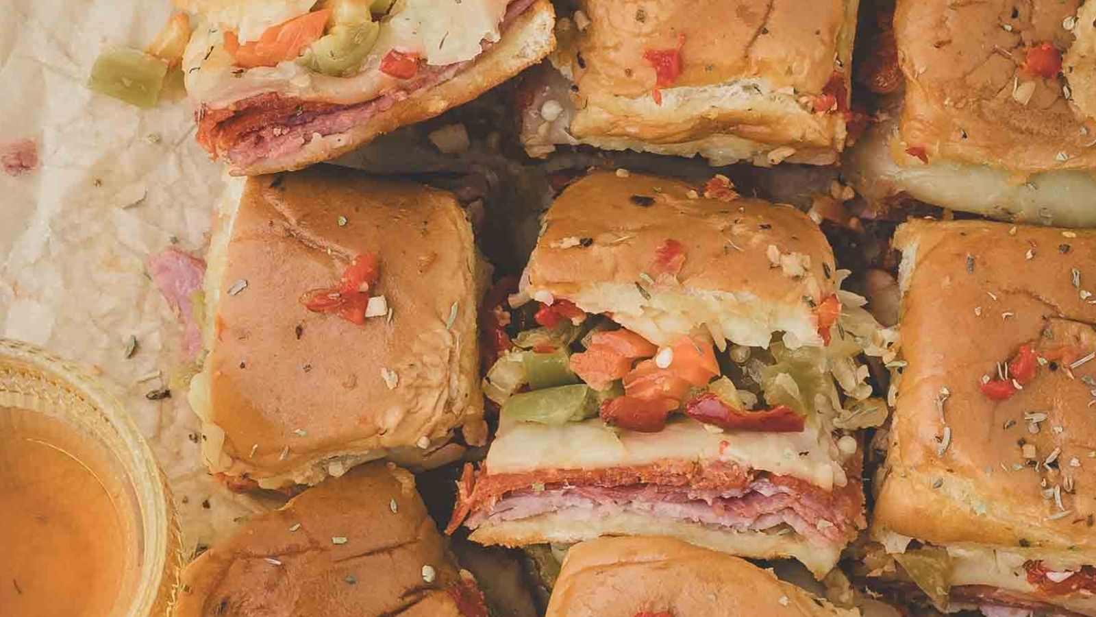 Hot Italian sub sliders layered with salami, pepperoni, ham, melted provolone, and banana peppers on toasted rolls.