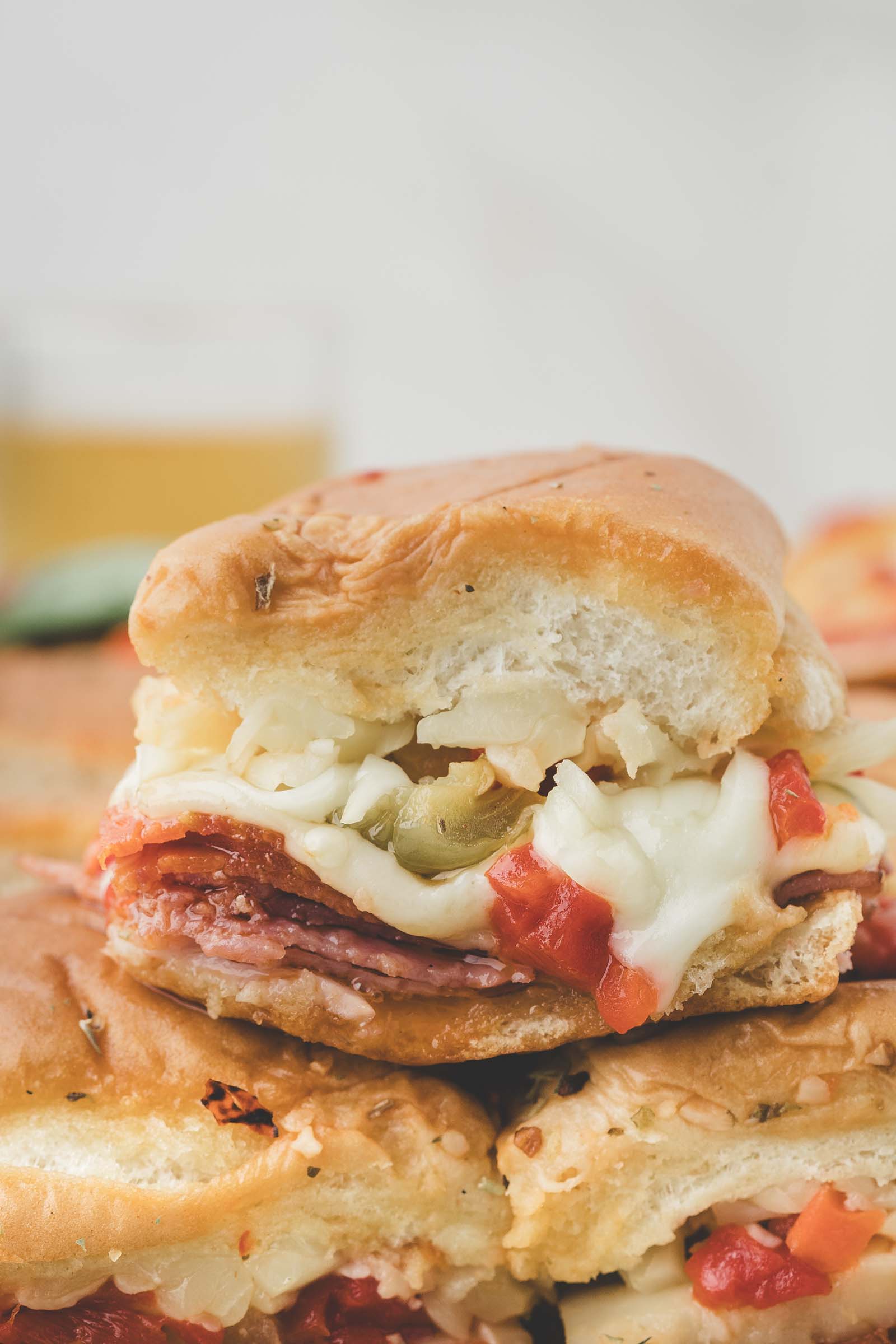 A close-up of a hot Italian sliders with melted cheese, sliced meats, giardiniera, and diced peppers on a soft bun.