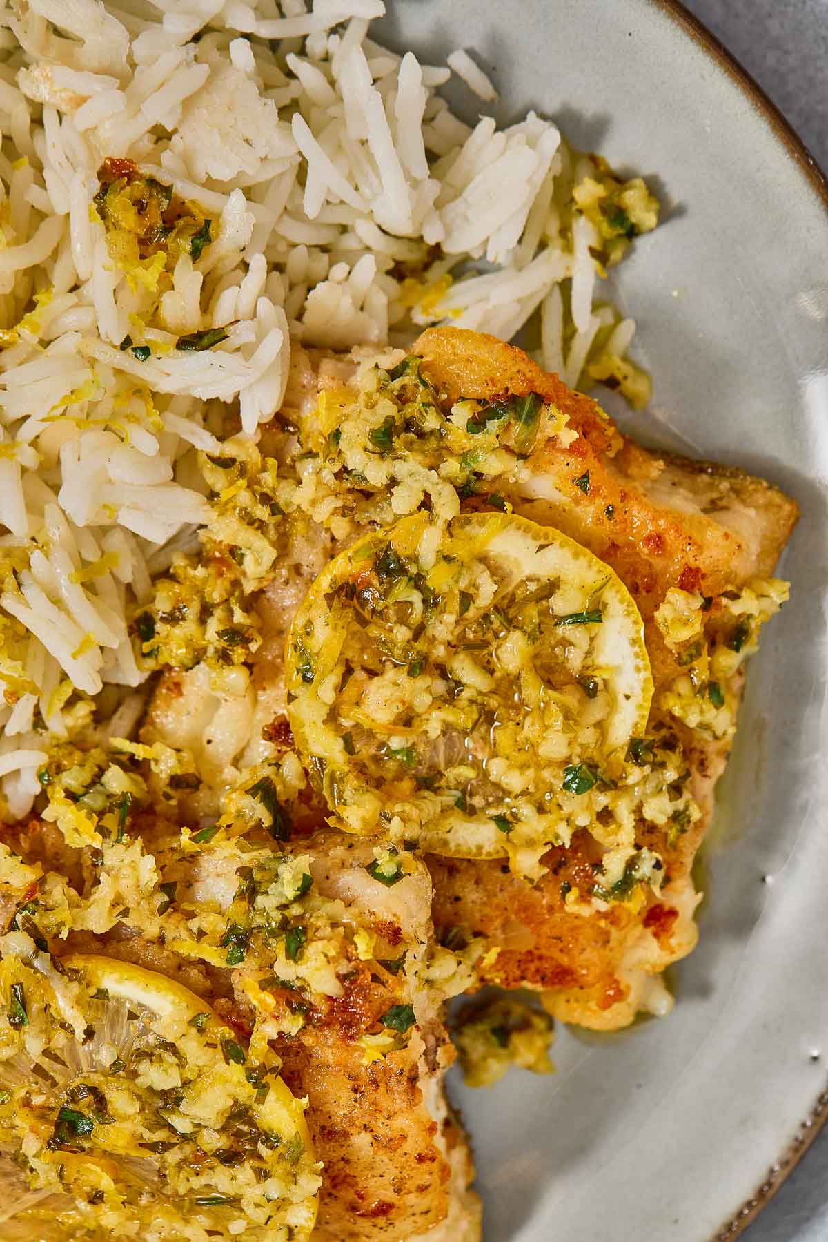 A plate pan seared cod with a garlic lemon butter sauce topped with lemon slices.