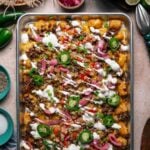 A sheet pan of loaded tater tots topped with ground beef, melted cheese, jalapeños, pickled onions, pico de gallo, green onions, and drizzled with sour cream.