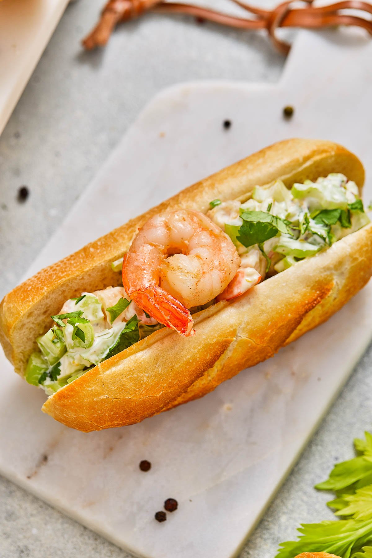 A sandwich roll filled with creamy shrimp salad and herbs on a marble cutting board.