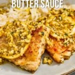 Close-up of pan seared cod fillets topped with garlic lemon butter sauce and lemon slices on a plate, with text detailing the recipe.