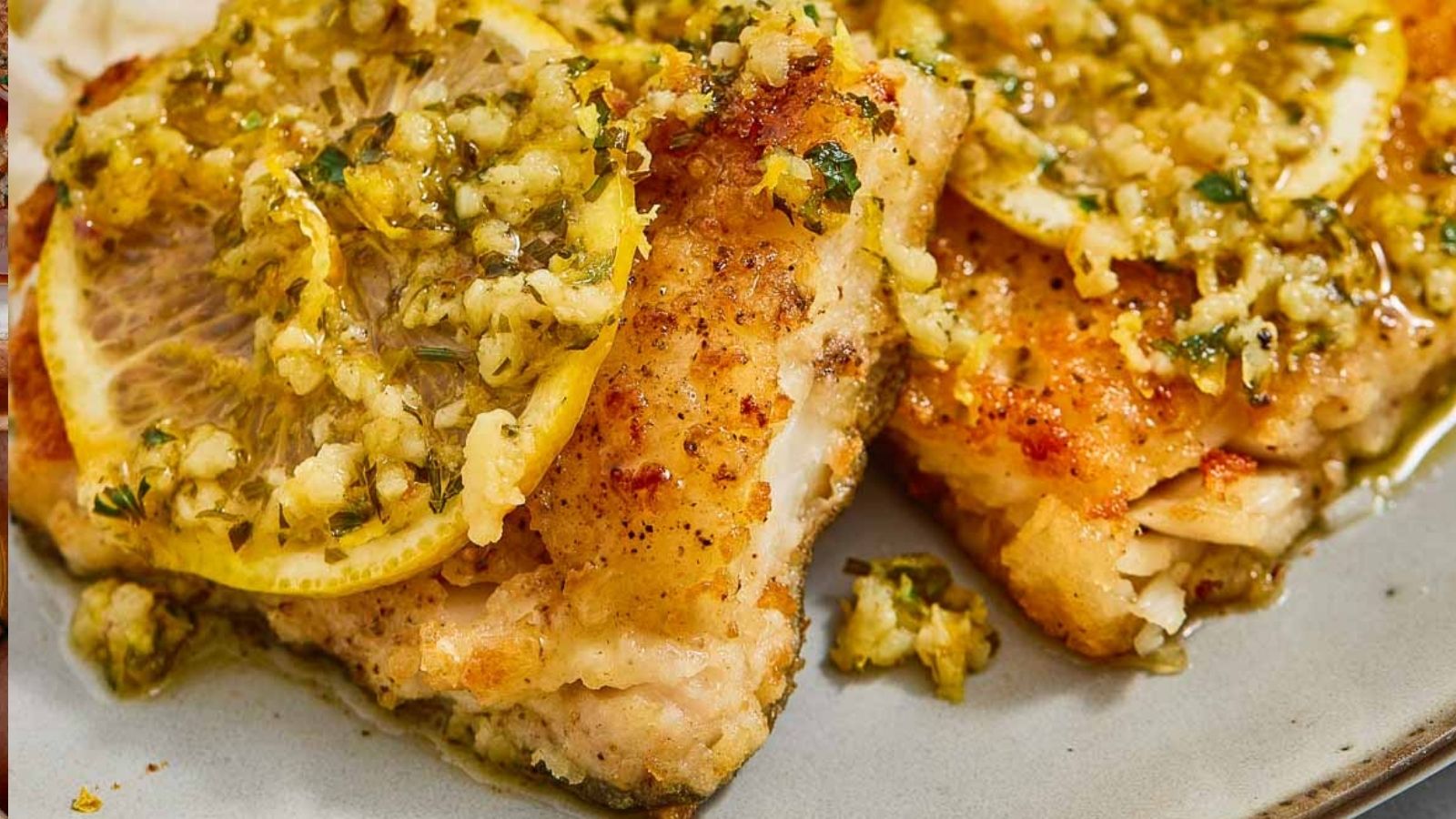 Two pieces of baked fish topped with lemon slices and a garlic herb sauce are served on a plate.