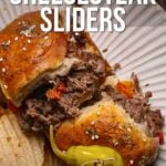 A Philly cheesesteak slider with shredded beef, melted cheese, and peppers in a bun, served on a plate with potato chips and a pepper. Recipe info at girlcarnivore.com.