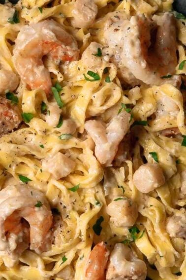 A bowl of fettuccine pasta topped with shrimp, scallops, creamy sauce, and chopped herbs.