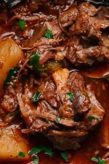 A bowl of beef stew with chunks of beef, potatoes, and vegetables in a rich brown broth, garnished with chopped herbs, and a spoon in the bowl.