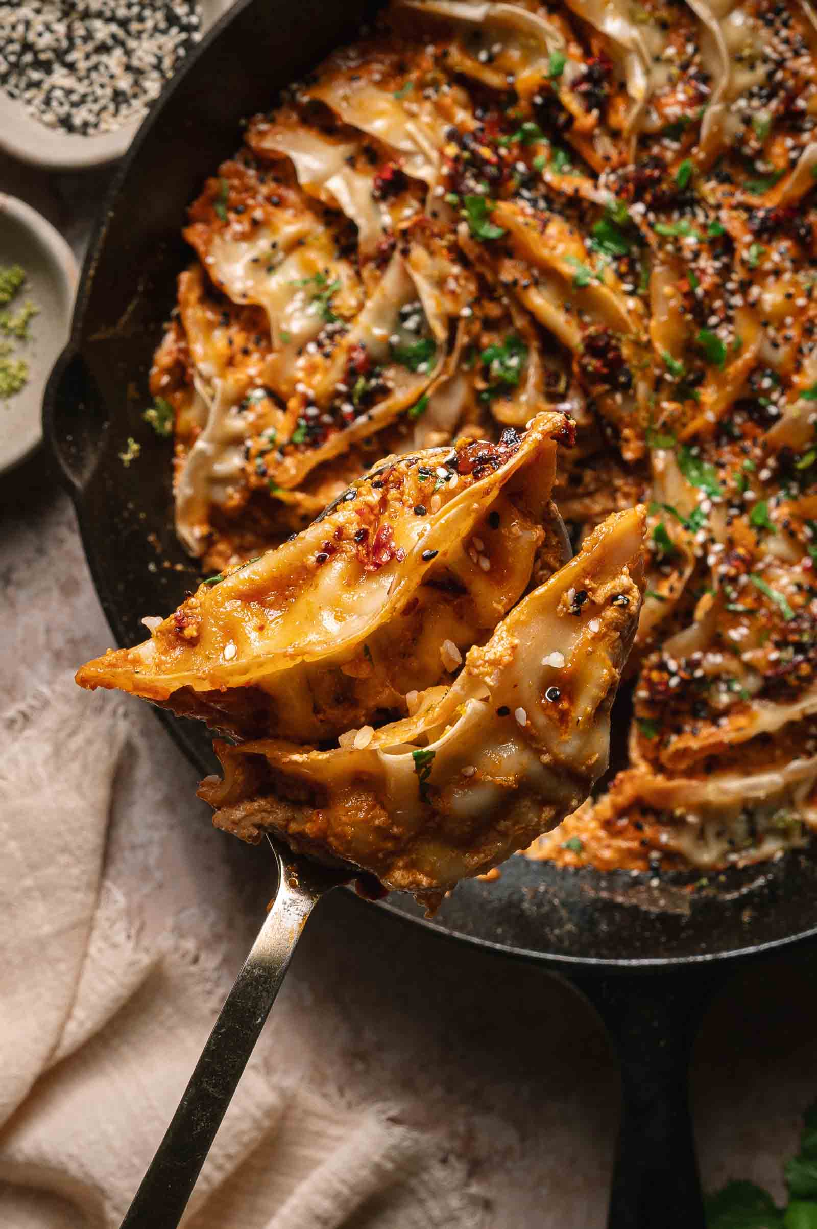 A close-up of viral baked dumplongss covered in coconut curry sauce, being lifted from a skillet with a serving spoon.