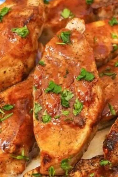 Grilled chicken breasts garnished with chopped parsley, arranged on a plate with a basting brush and a blue checkered napkin nearby.