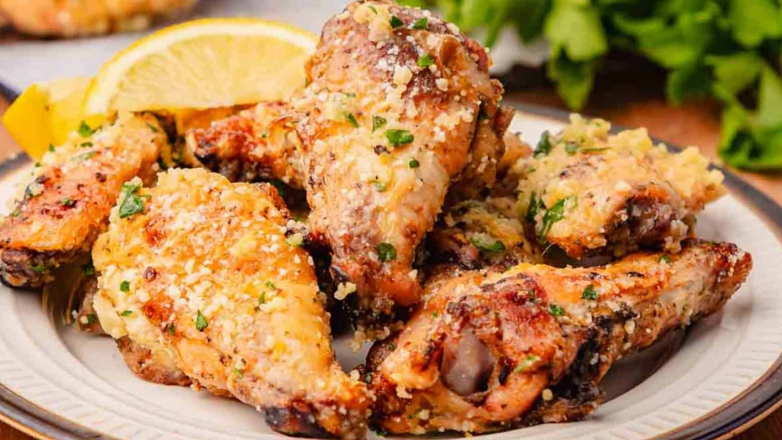 A plate of crispy garlic parmesan chicken wings garnished with herbs and served with lemon wedges.