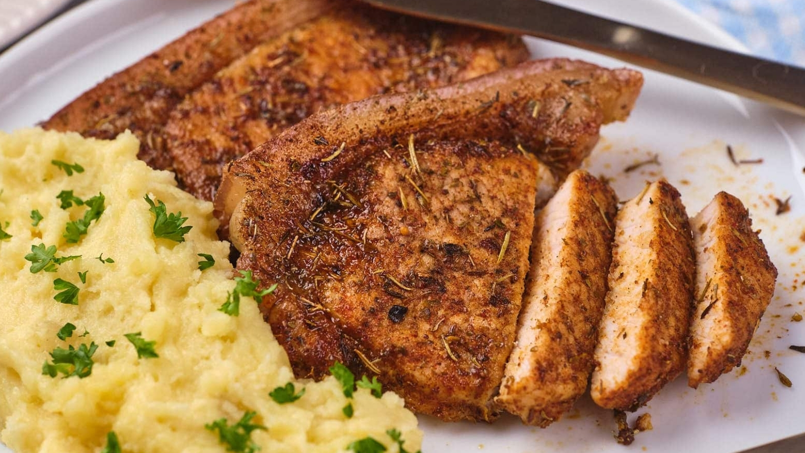 A serving of seasoned pork chops with a side of mashed potatoes on a white plate.