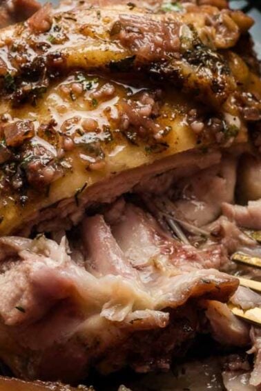 A close-up of a cooked piece of seasoned pork being pulled apart with a fork on a black plate, with sliced apples on the side—perfect for hearty dinners.