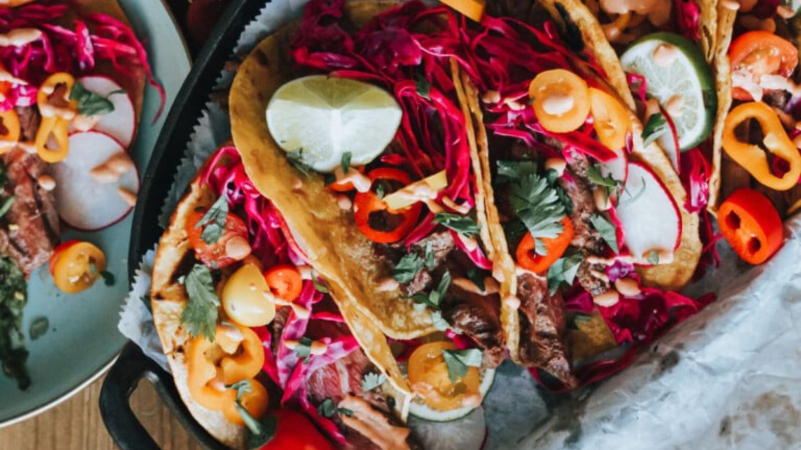 Bavette steak tacos topped with onions, cilantro, and lime wedges.