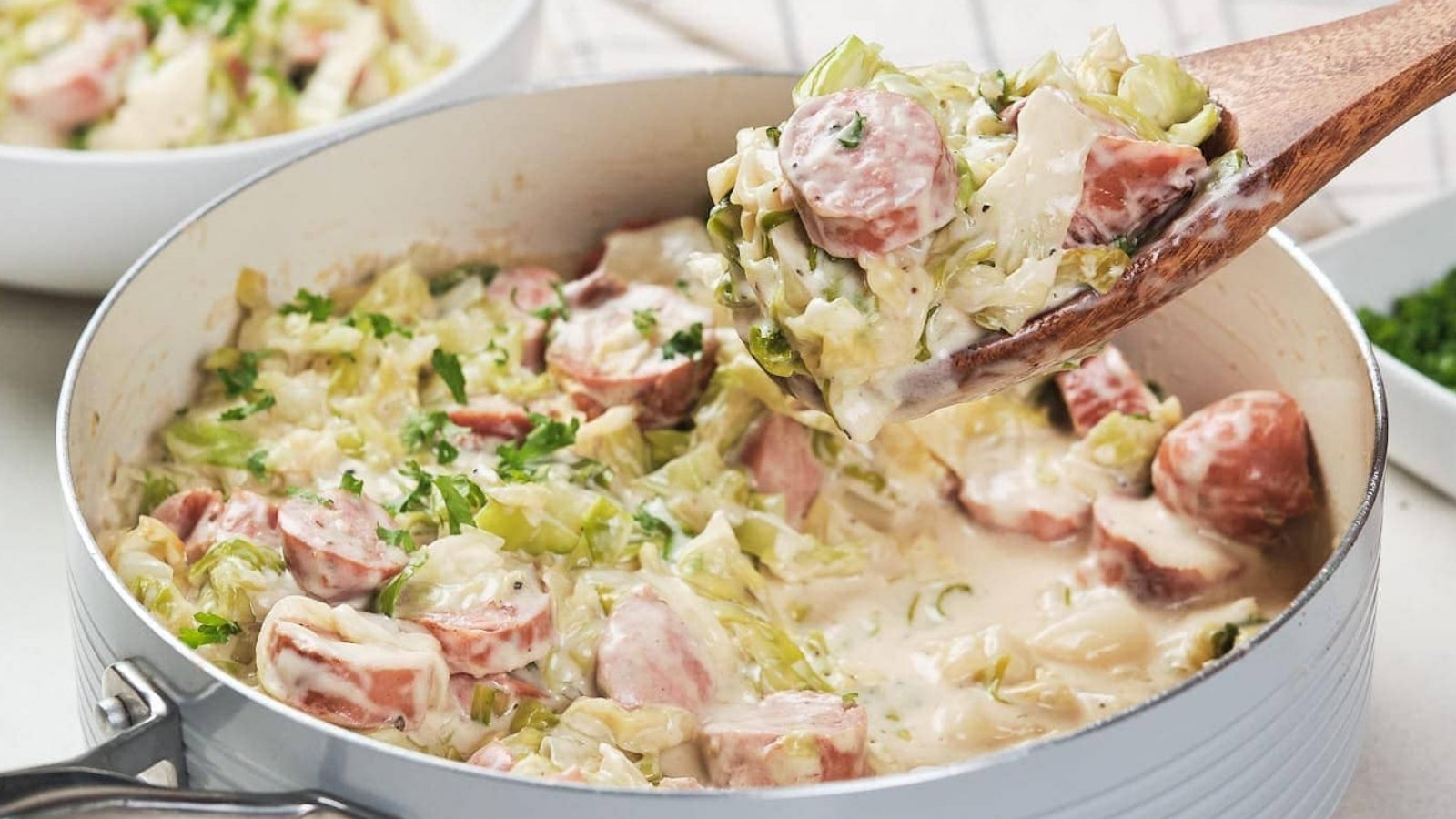A skillet containing a creamy cabbage and sausage alfredo garnished with herbs.