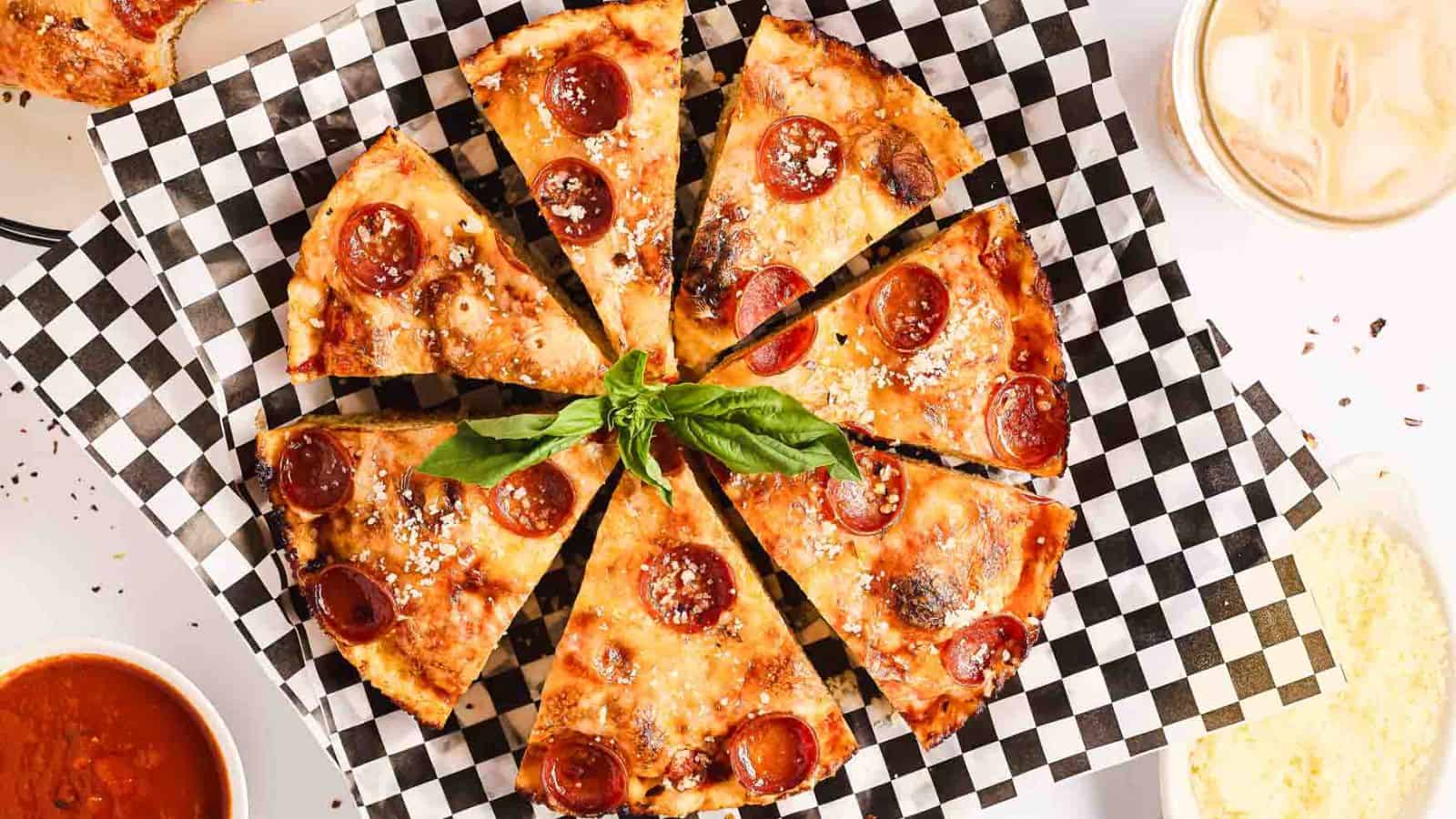 Sliced pepperoni pizza on a checkered platter garnished with fresh basil.
