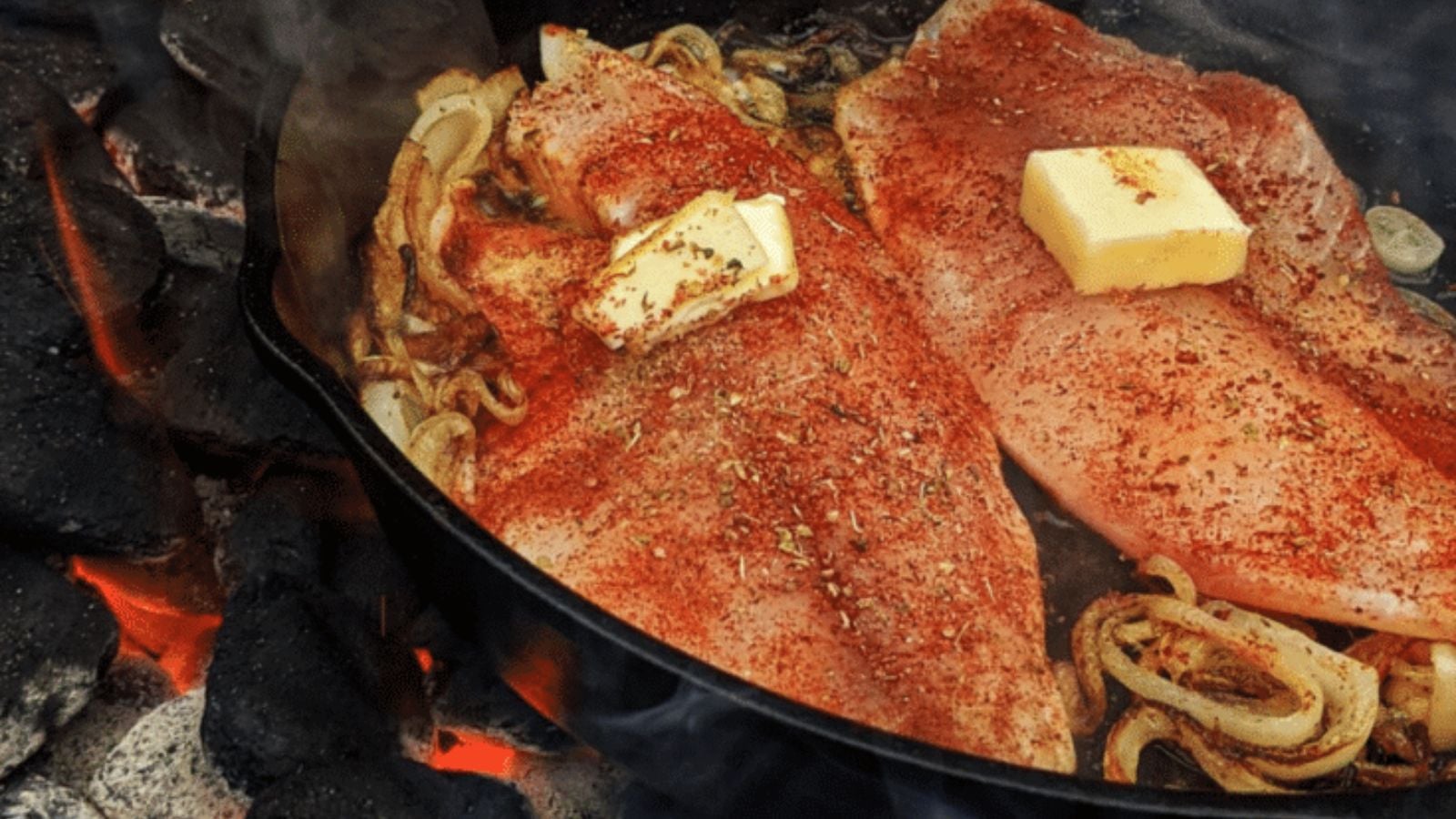 Tilapia grilled over charcoal with dark grill marks and lemon wedges beside it.