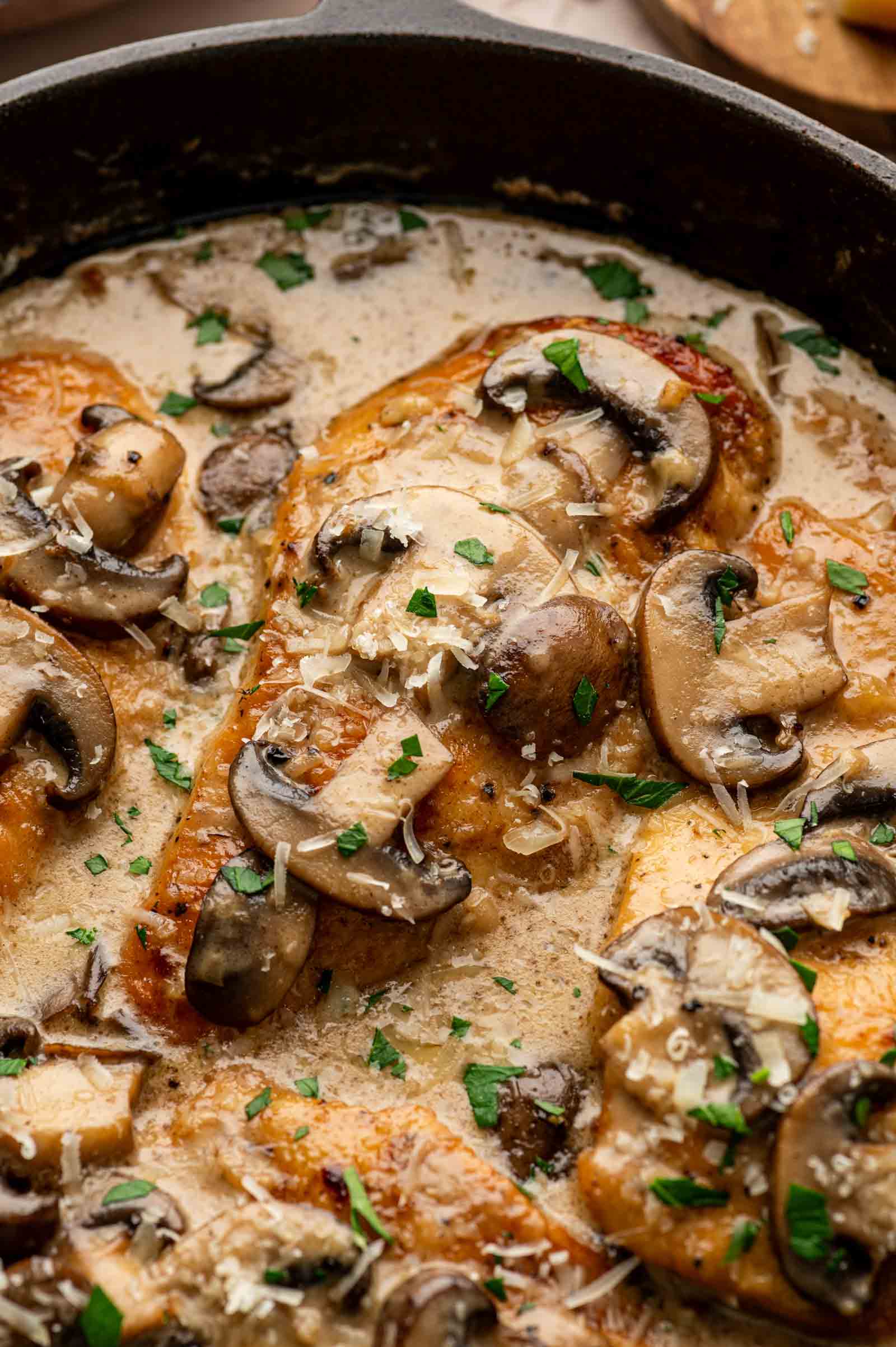 Chicken breasts cooked in a creamy sauce with sliced mushrooms and garnished with chopped parsley in a skillet.