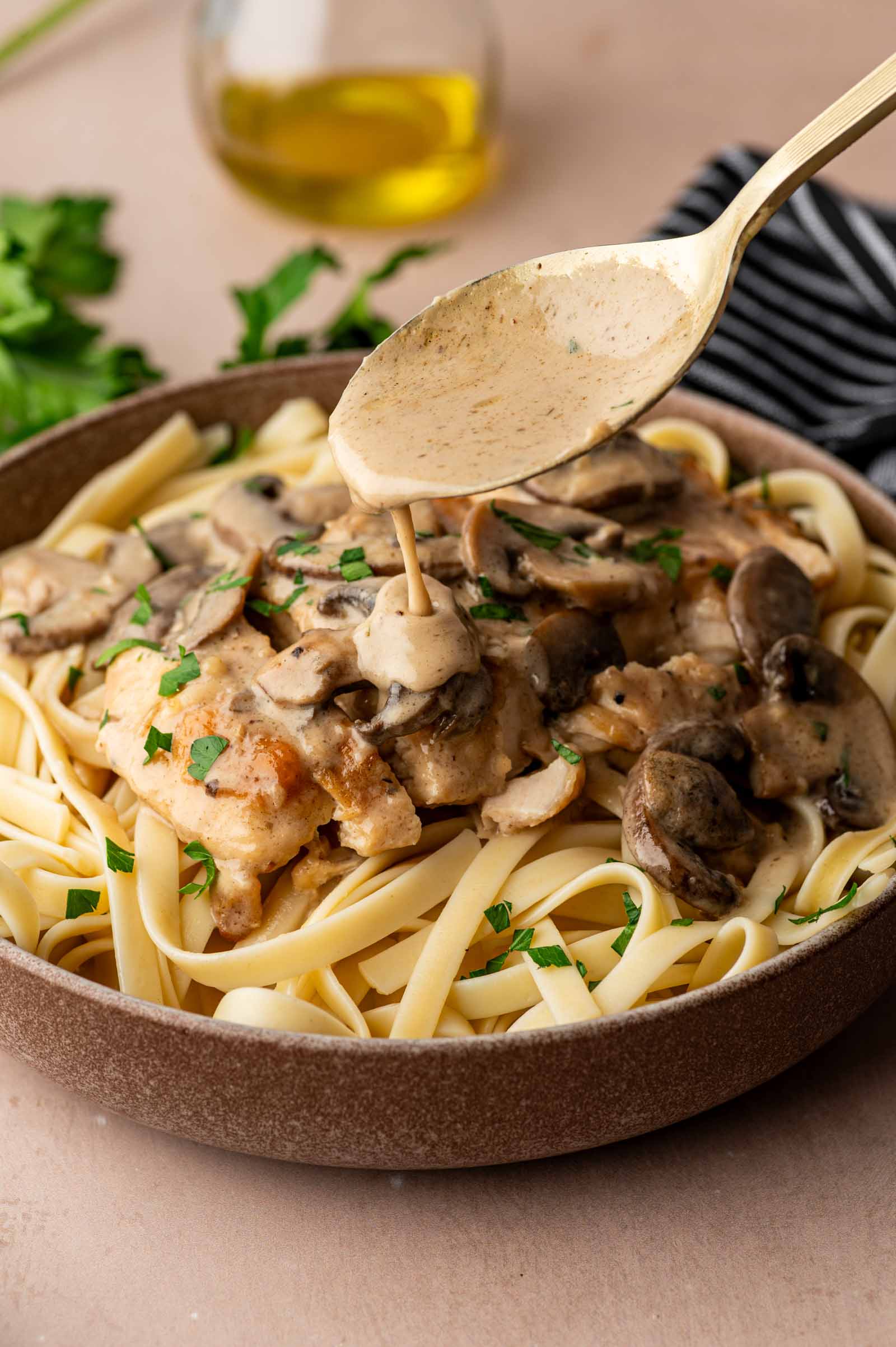 A plate of fettuccine topped with chicken marsala being spooned over, garnished with chopped parsley.