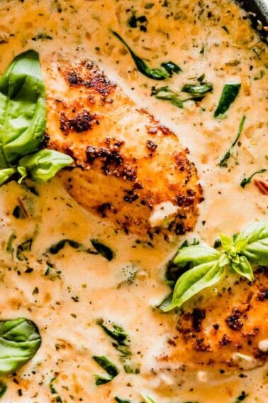 Three pieces of seared chicken breast in a creamy herb sauce with spinach, garnished with fresh basil, served in a skillet.