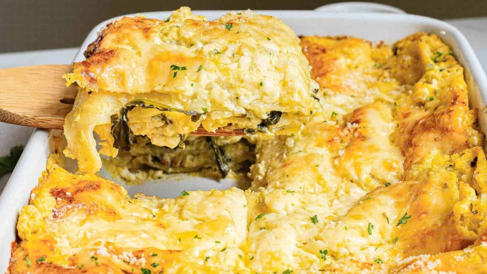 A serving of cheesy lasagna is being lifted from a baking dish, revealing layers of pasta, sauce, and cheese.