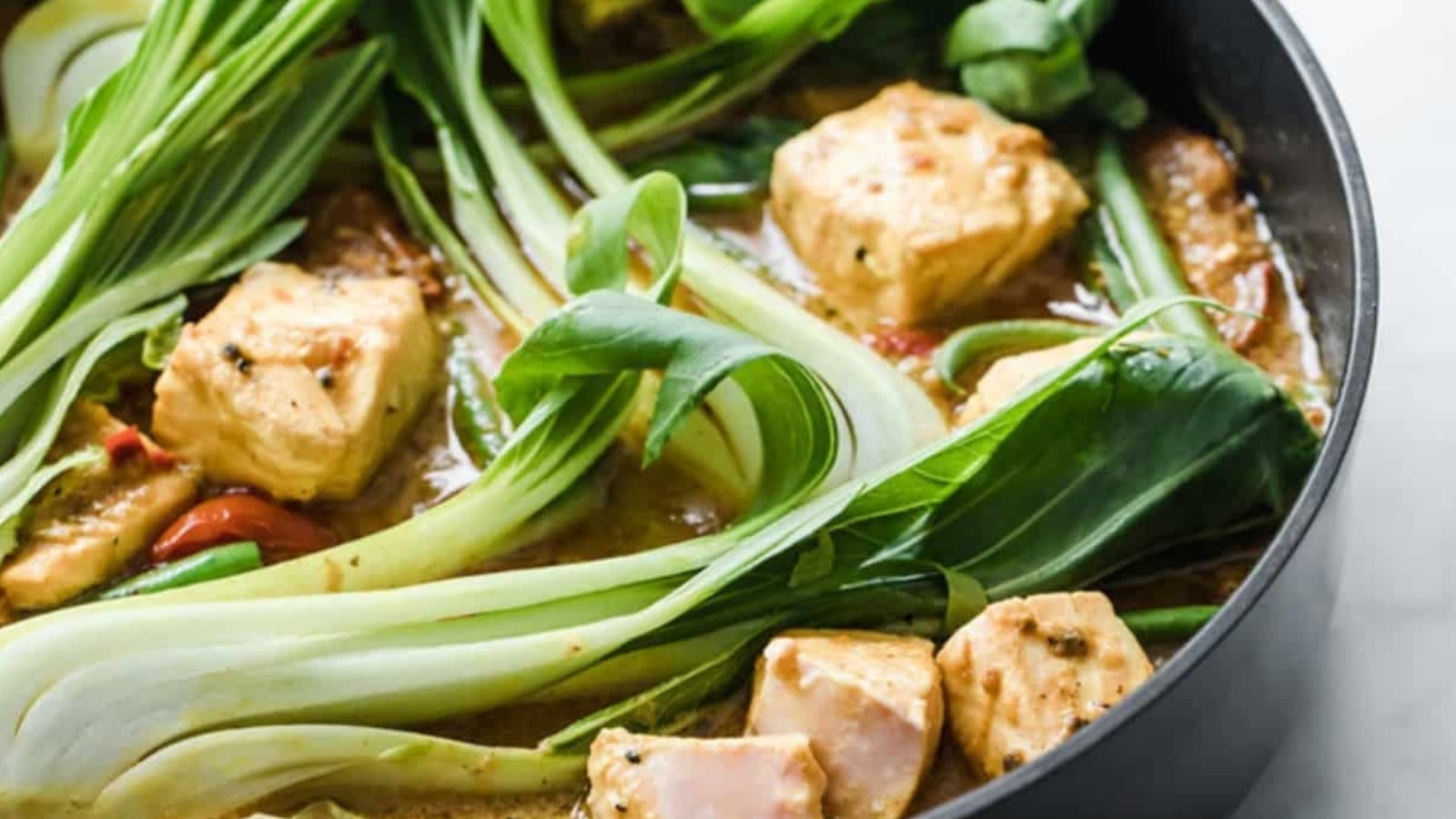 Curry salmon with coconut milk and bok choy in a bowl with a fork.
