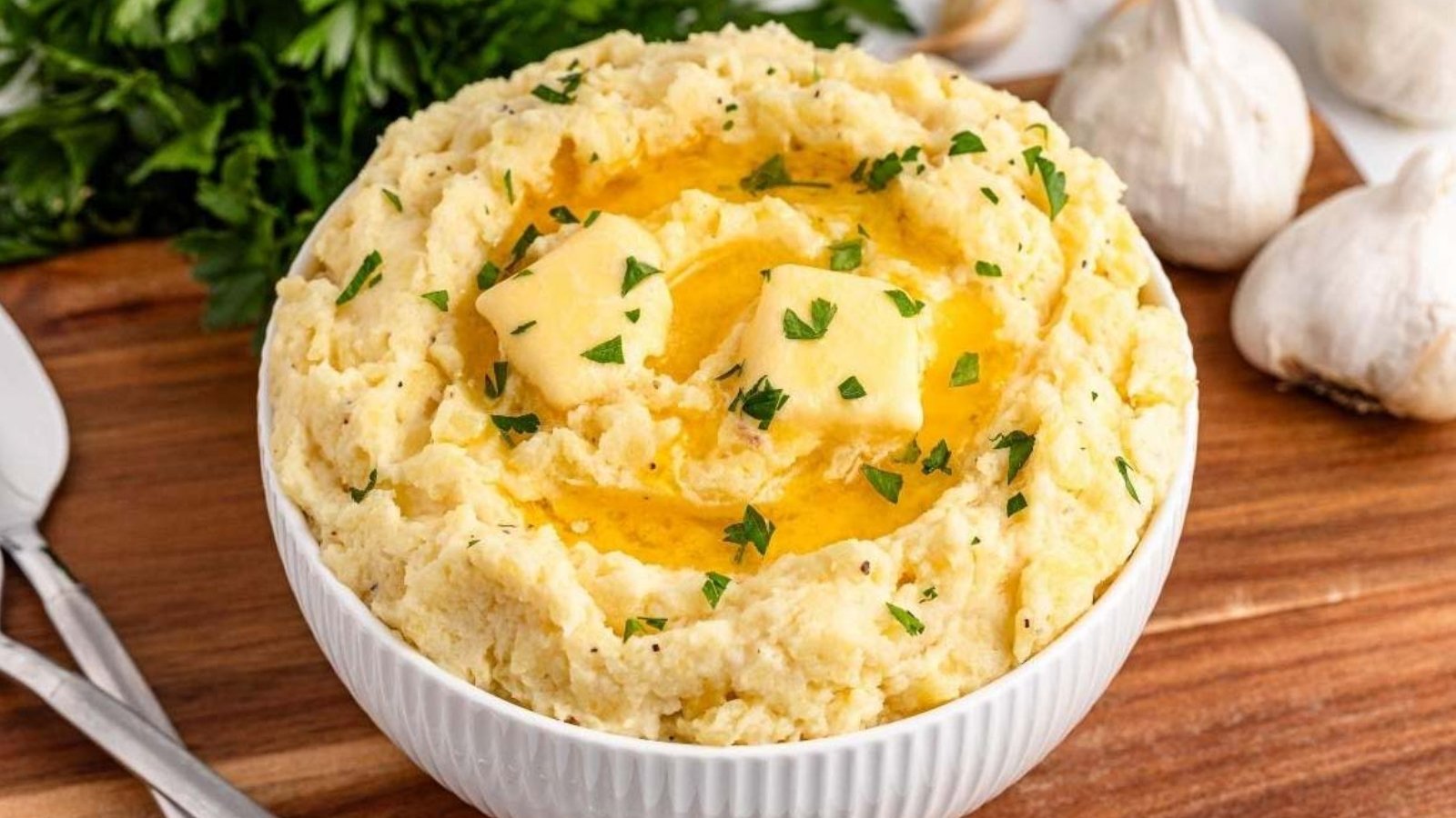 A bowl of garlic mashed potatoes topped with melted butter and chopped parsley.