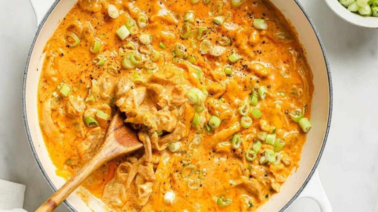 Green chile chicken in a pan with a wooden spoon.