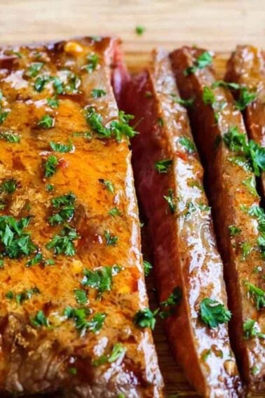 Sliced, cooked marinated steak topped with chopped parsley on a wooden cutting board.