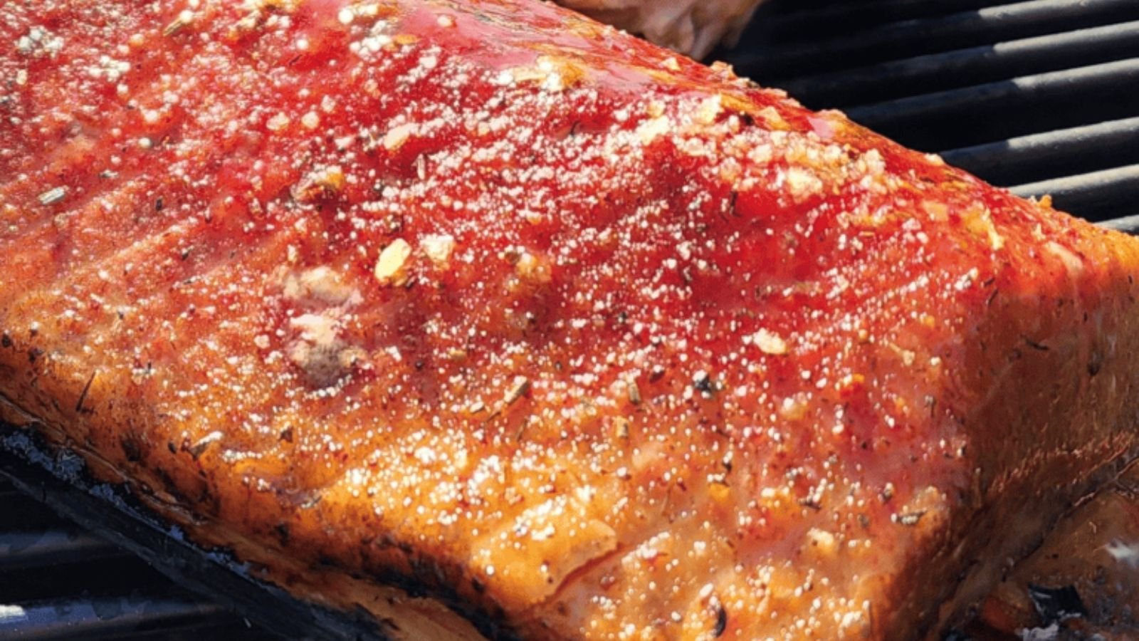 Cedar plank grilled salmon flaking with smoky edges and lemon slices across the plank.