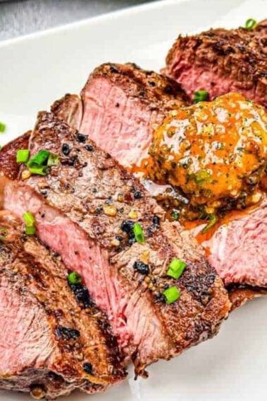Sliced medium-rare steak with a dollop of seasoned butter and chopped chives on a white plate.
