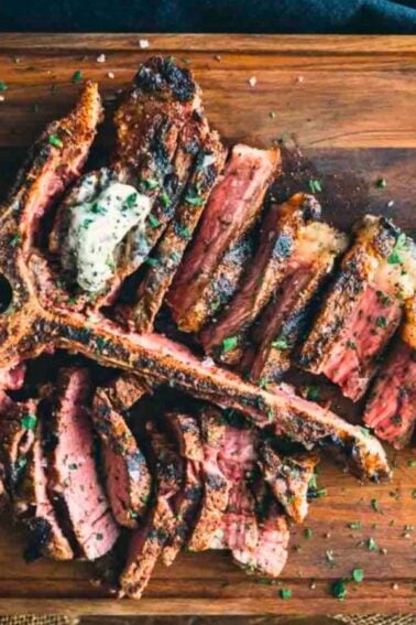 Sliced, grilled T-bone steak with a dollop of butter and herbs on a wooden cutting board.
