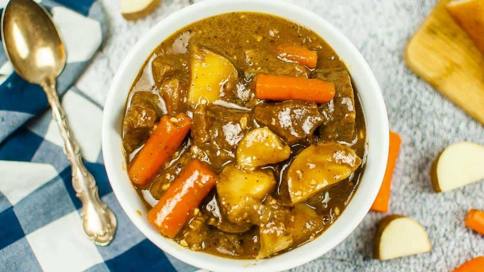 Top view of a bowl of Guinness beef stew with a black checked napkin and a spoon.