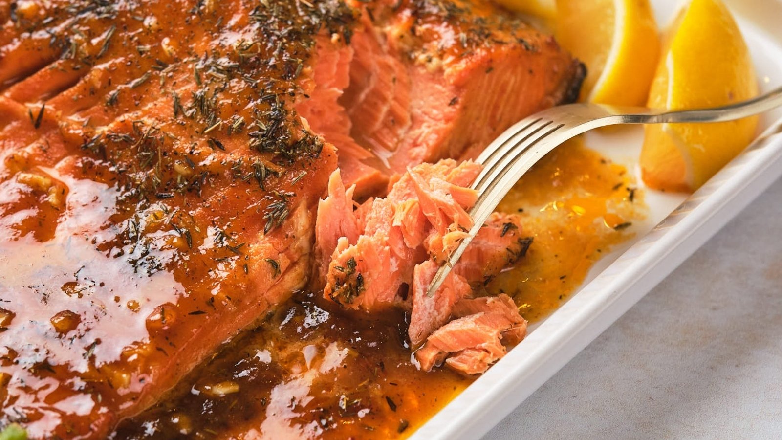 Honey mustard salmon with a glossy glaze, garnished with herbs and served with lemon wedges on a white plate.