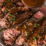 Sliced medium-rare steak topped with a1 sauce, garnished with chopped herbs, served on a plate with extra sauce in a small bowl.