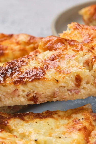A slice of impossible quiche being lifted from a whole quiche on a plate.
