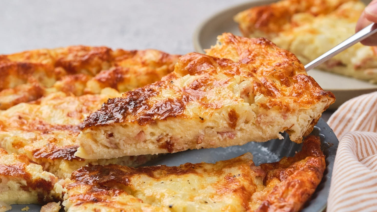 A slice of impossible quiche being lifted from a whole quiche on a plate.