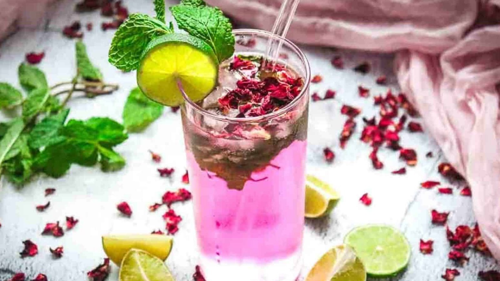 A pink drink with ice, mint, lime slice, and rose petals in a glass, garnished with fresh mint and lime.