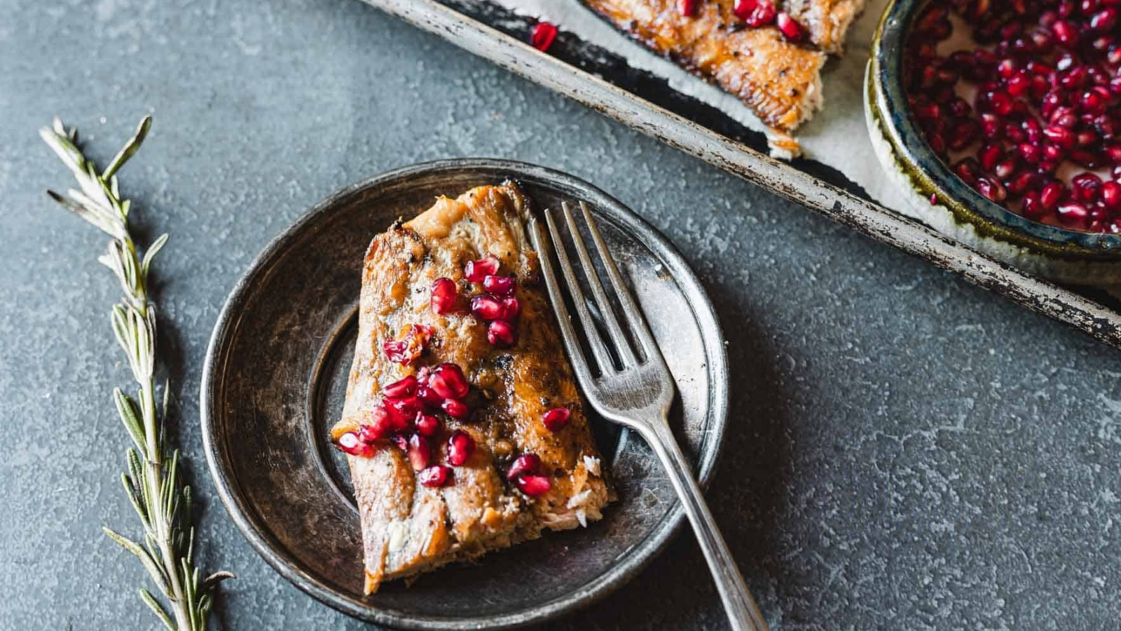 A plate with a piece of pomegranate glazed salmon garnished with pomegranate seeds and a fork.