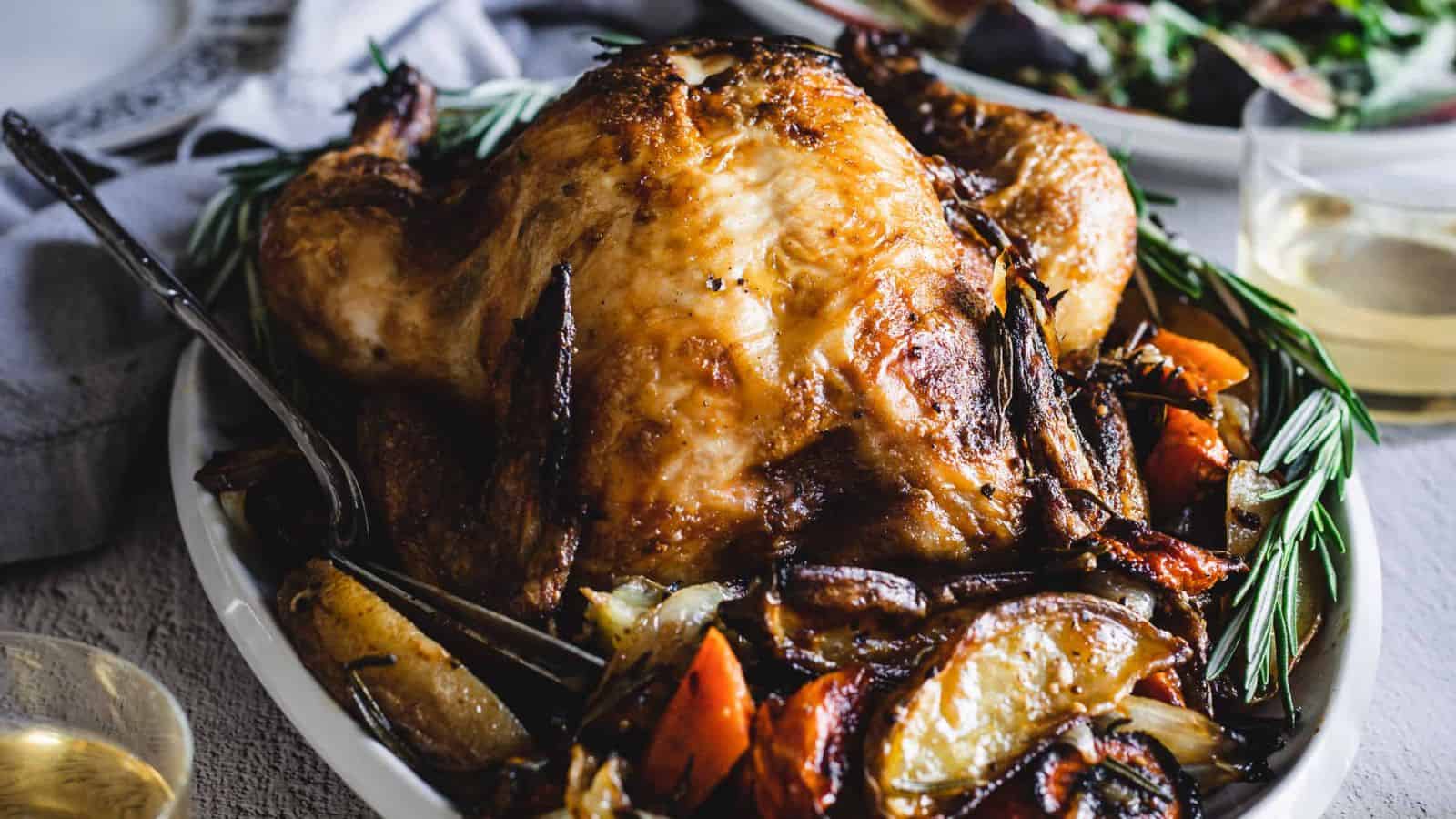 Hands holding paprika chicken and vegetables on a sheet pan.