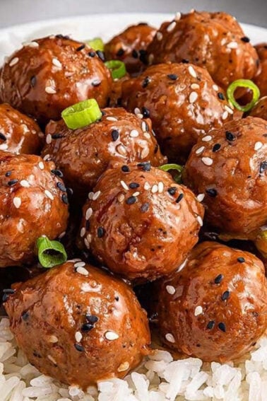 A white bowl filled with white rice, topped with glazed meatballs, sesame seeds, and chopped green onions; a fork is placed beside the bowl.