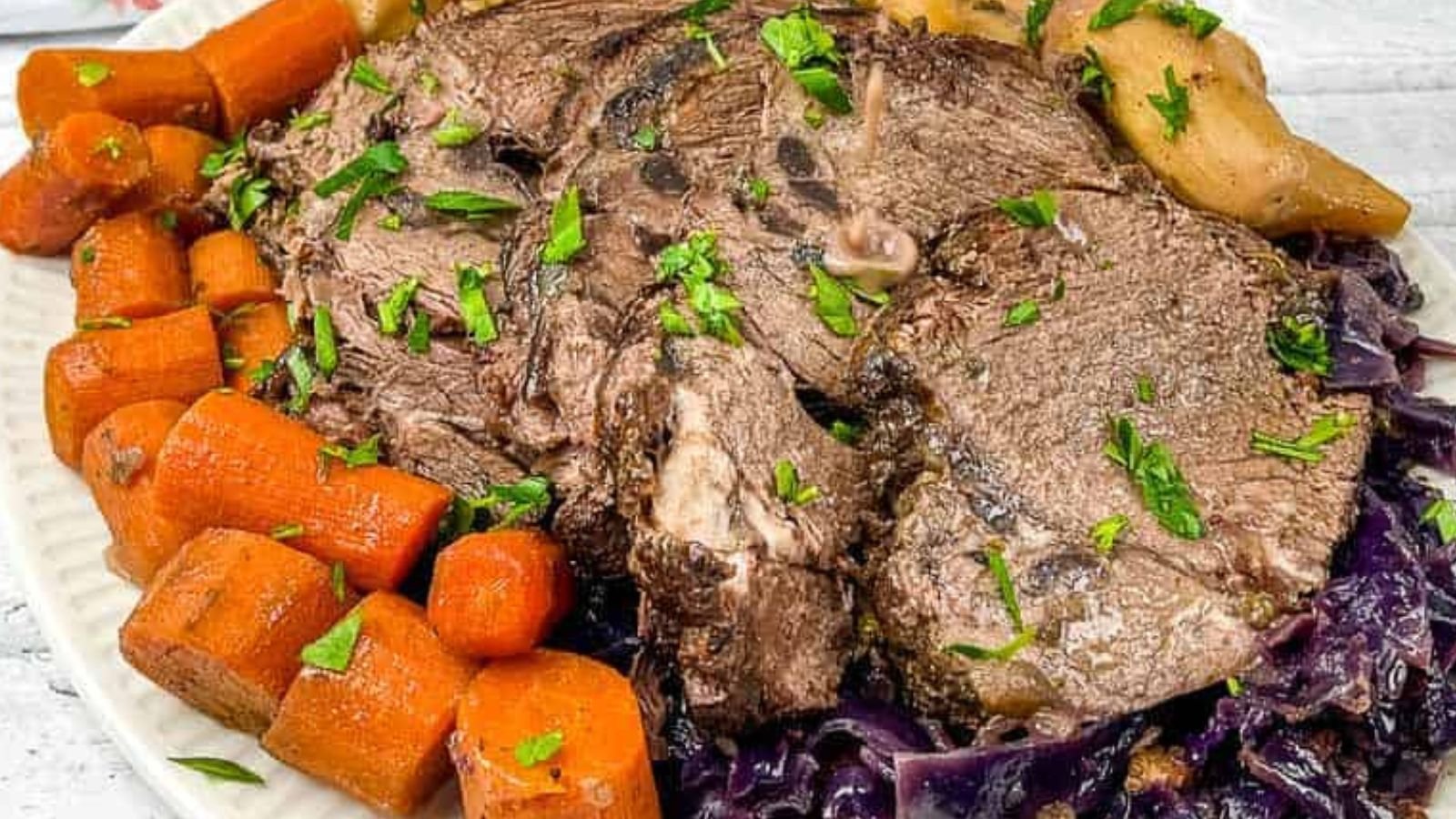 A plate with sliced pot roast, cooked carrots, potatoes, and cabbage, garnished with chopped parsley.