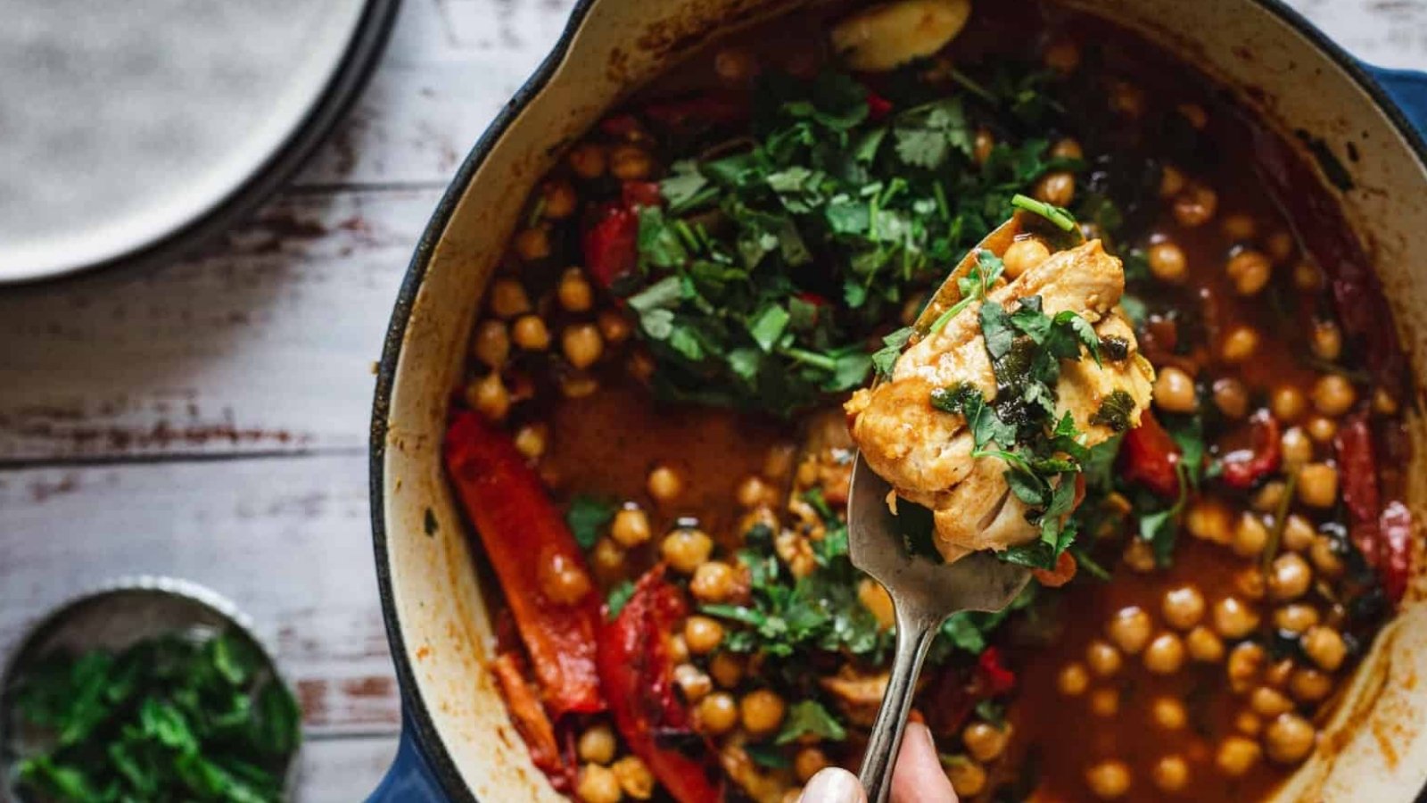 A fork holds a bite of chickpea stew with herbs above a pot filled with stew, chickpeas, and greens.