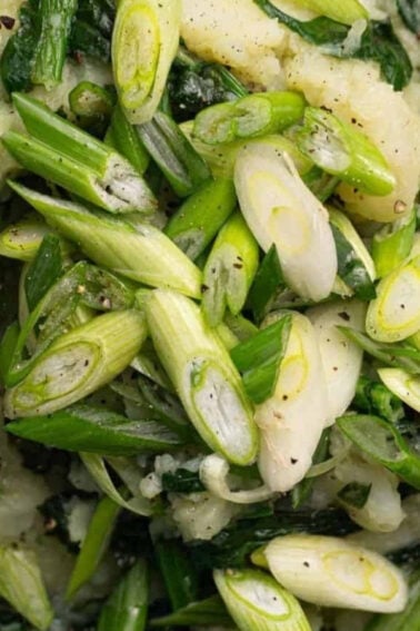 A close-up of mashed potatoes mixed with chopped greens and topped with sliced scallions in a bowl.