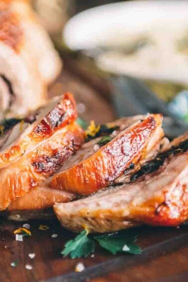 Sliced roast meat is arranged on a wooden cutting board with serving utensils, with various side dishes visible in the background—perfect for sharing as part of your Valentine’s Recipes.
