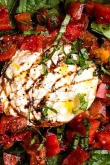 A plate of fresh spinach topped with diced tomatoes, burrata cheese, chopped herbs, and a drizzle of balsamic glaze.