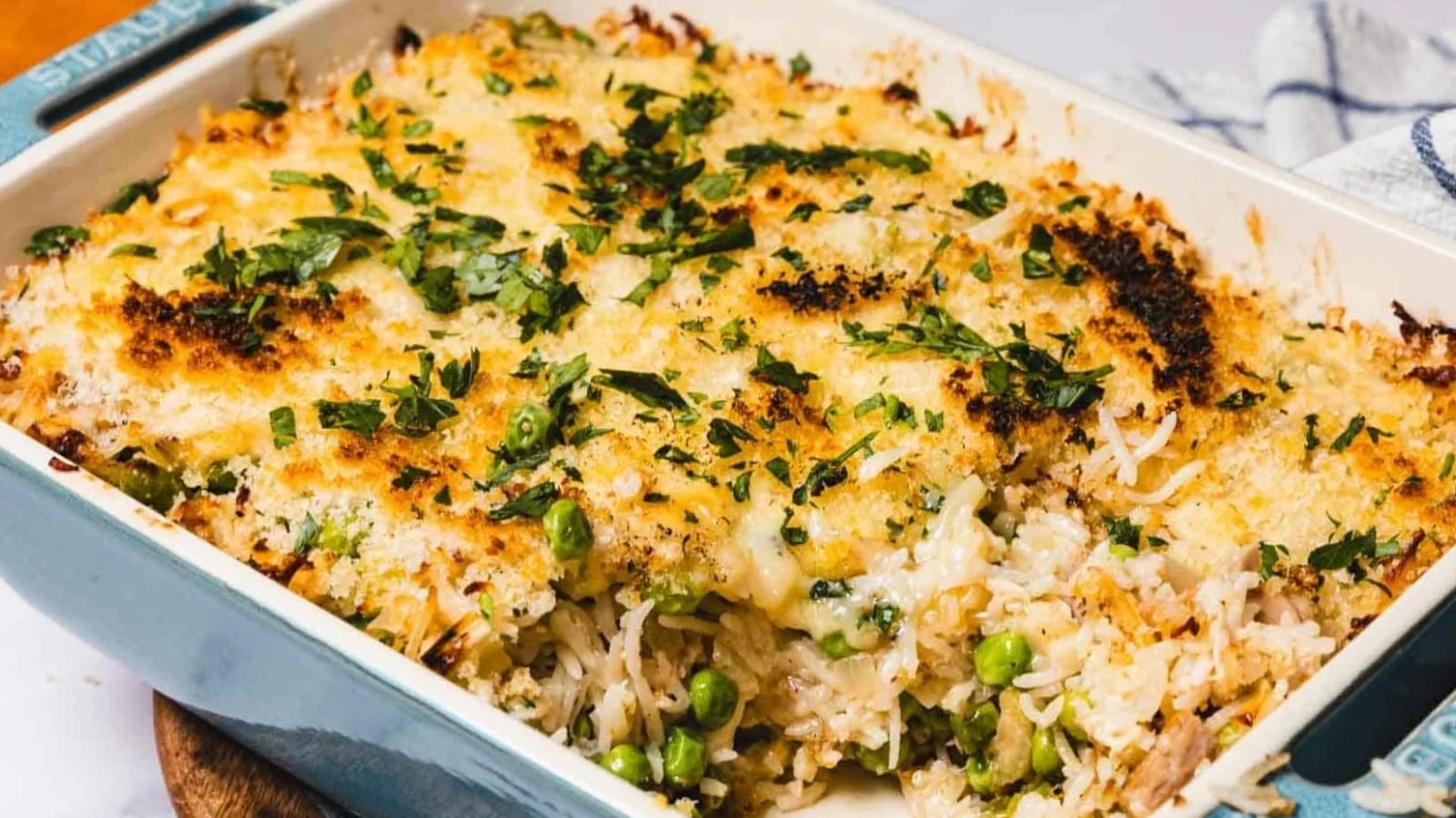 A baked casserole topped with melted cheese and herbs, with rice and green peas visible inside.