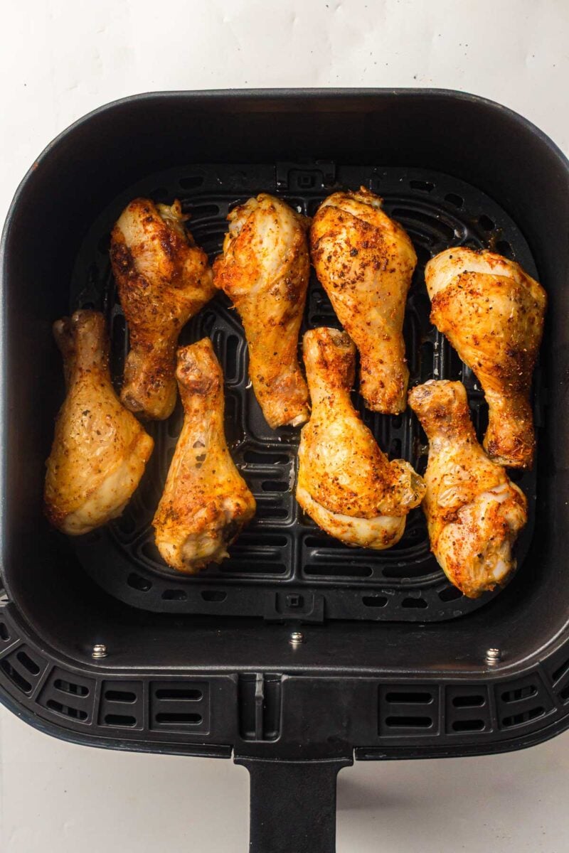 Eight seasoned chicken drumsticks arranged in a single layer inside an air fryer basket.
