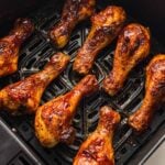 Eight glazed chicken drumsticks are arranged in a single layer inside the basket of an air fryer, cooked to a golden brown.